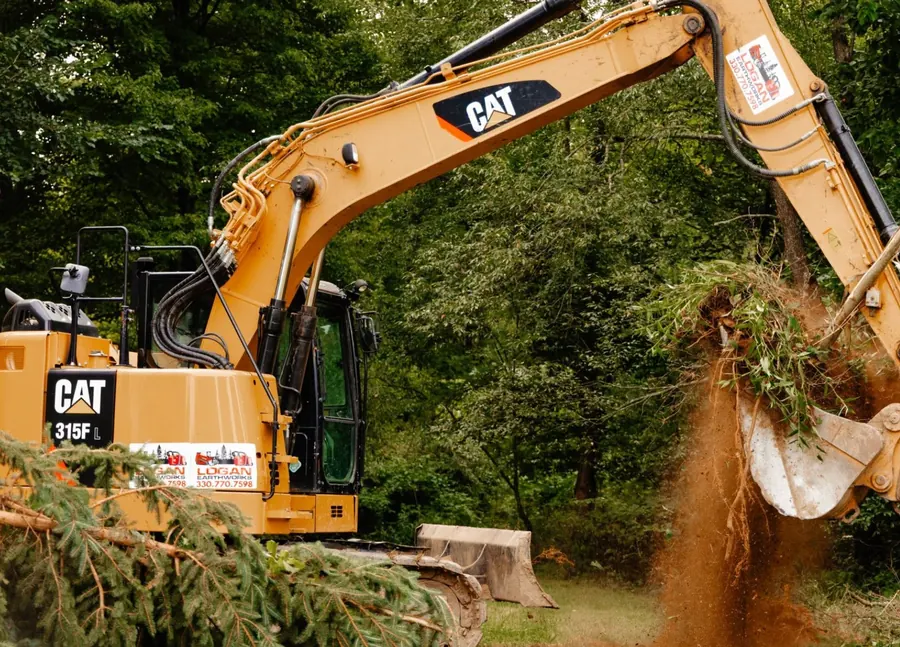 CAT excavator with Logan Earthworks decals shaking dirt from an uprooted bush