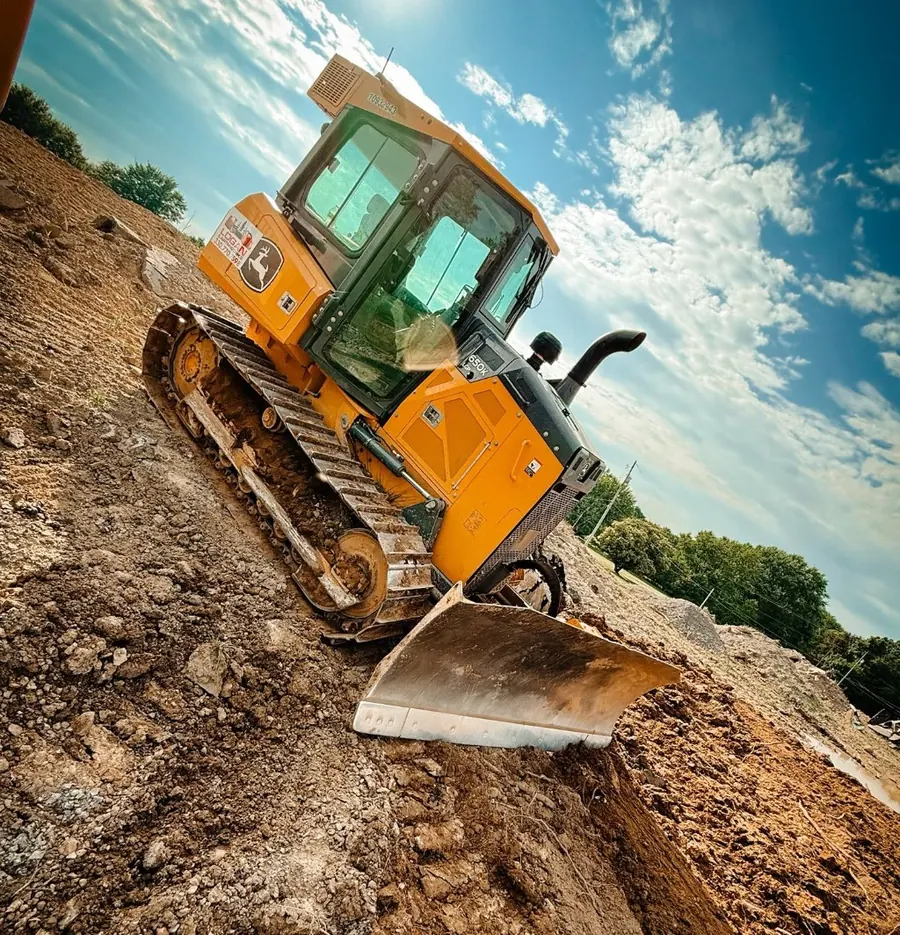 Dozer with a Logan Earthworks decal cutting a dirt slope under blue sky