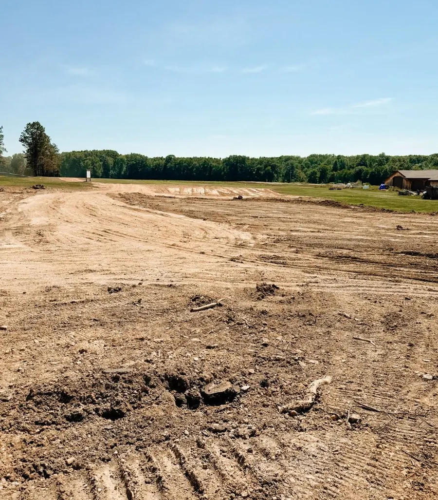 Wide dirt pad graded smooth across an open field with a treeline behind